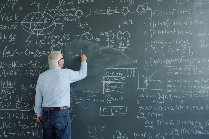 Matematyk sprawdzający równania i zapisany dowód na tablicy